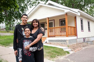 A mom and her two sons posing in front of their home, smiling