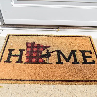 Home mat outside house with Minnesota shape and moose.