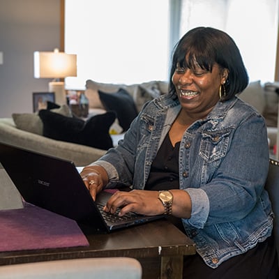 Angela smiling and using a laptop in her home.
