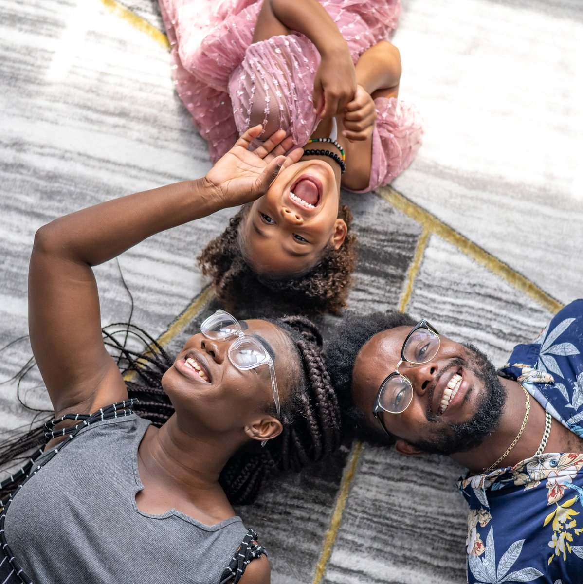 A woman, a man, and small child laying on the floor and laughing