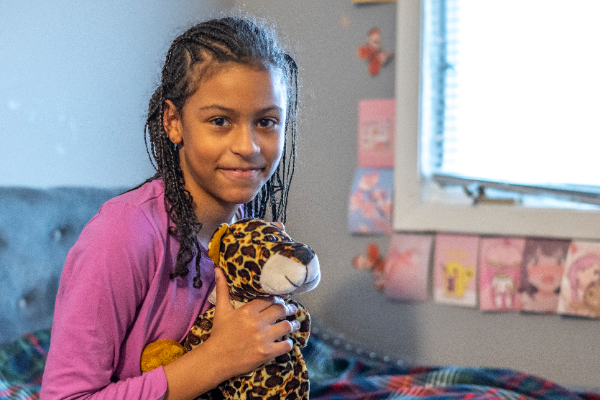 Layla Joy sitting on her bed holding a stuffed giraffe.