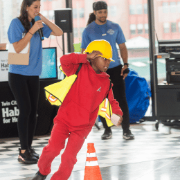 A child wearing hard hat and safety vest running around orange pylons during a game.