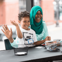 A mother and child waving from a craft table.